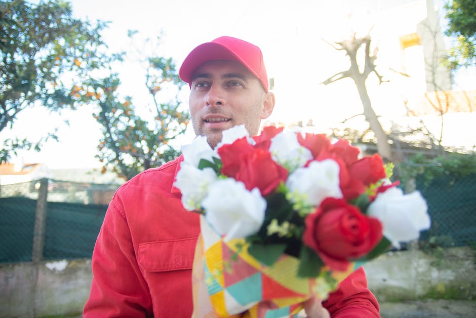 A delivery person in a red uniform and matching cap holding a vibrant bouquet of fresh flowers in front of them, with prominent red roses and white blossoms arranged in a colorful wrapper. The person 